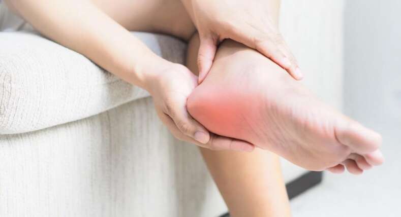 Persona sentada sujetando pie con síntomas de dolor e inflamación característicos de la fasctitis plantar