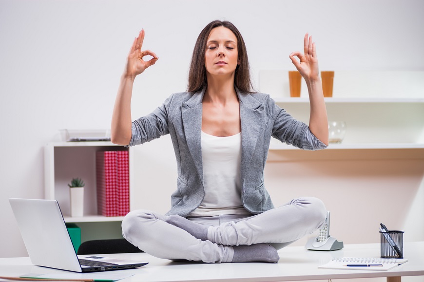 Mujer sentada sobre mesa de trabajo con piernas cruzadas haciendo yoga para el estrés