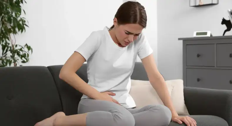 Mujer recostada en un sofá con expresión de dolor pélvico agudo, característico de la neuralgia del nervio pudendo.