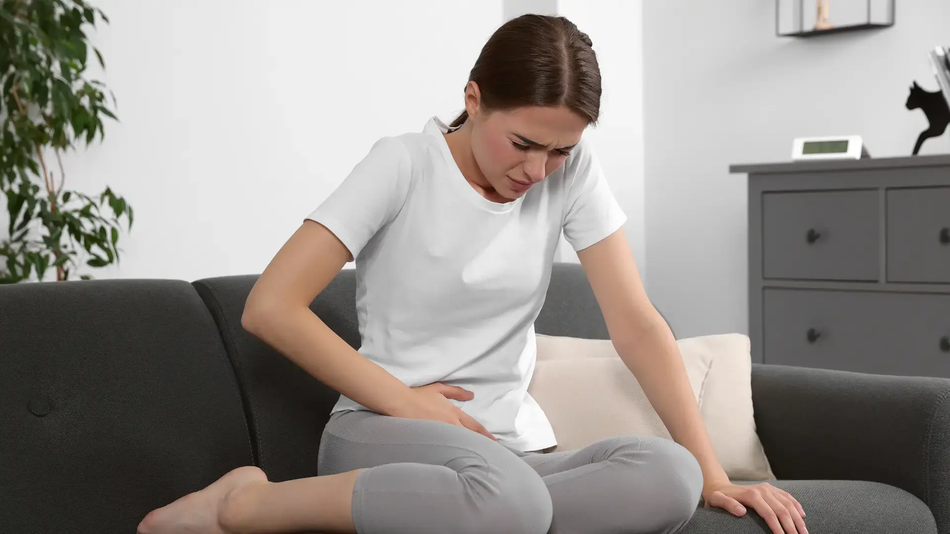 Mujer recostada en un sofá con expresión de dolor pélvico agudo, característico de la neuralgia del nervio pudendo.